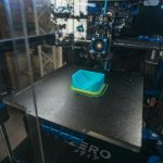 Close-up of a 3D printer creating a plastic object in an industrial setting.