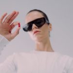 Modern woman in sunglasses holding a red pill in a futuristic setting. Perfect for healthcare or sci-fi themes.