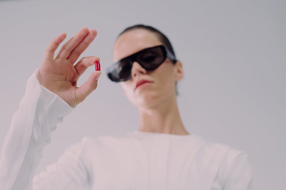Modern woman in sunglasses holding a red pill in a futuristic setting. Perfect for healthcare or sci-fi themes.