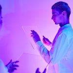 Two individuals engaging with futuristic transparent touch screens in a vibrant purple-lit studio.