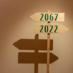 <h1>The Future of Navigation: Decentralized Geo-Spatial Intelligence for Autonomous Vehicles</h1> Wooden signpost indoors pointing to years 2067 and 2022, casting shadows.