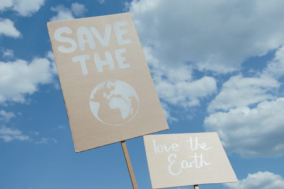 Protest signs promoting environmental conservation against a cloudy blue sky.