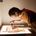 <h1>The Future of Tangible Computing: Decentralized Metamaterials Protocols for HCI</h1> A photographer inspects film negatives on a light table in a dimly lit room.