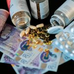 The Hidden Health Costs of Fast Fashion and Corporate Strategy A still life of supplements, pills, and currency with a dark backdrop.