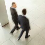 The High-Performance Trap: Managing Addiction in Executive Wellness Overhead view of two blurred businessmen walking in an office corridor.