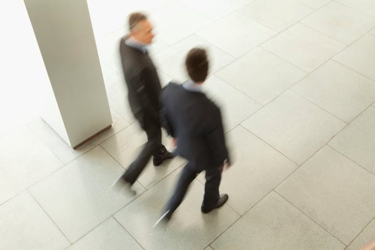Overhead view of two blurred businessmen walking in an office corridor.