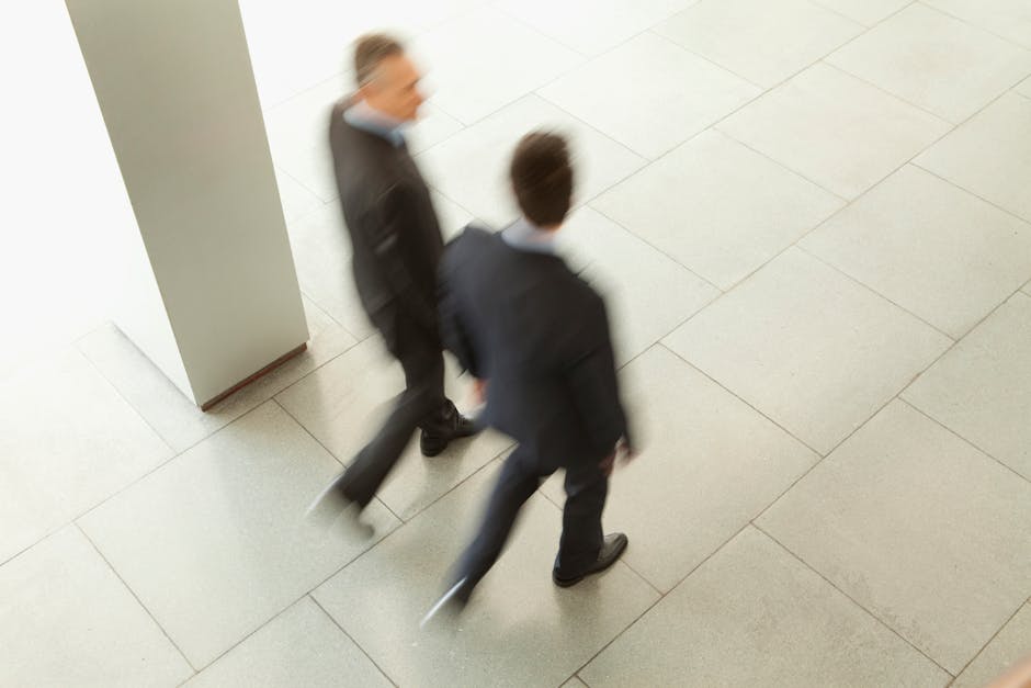 Overhead view of two blurred businessmen walking in an office corridor.
