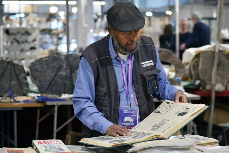 Man wearing a hat and vest browsing vintage books at an indoor market.