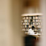 A student intensely focused on work in a library surrounded by bookshelves.