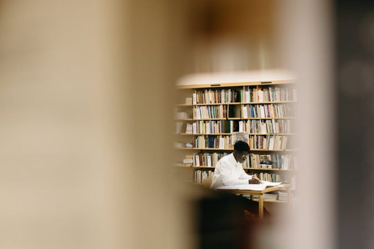 A student intensely focused on work in a library surrounded by bookshelves.