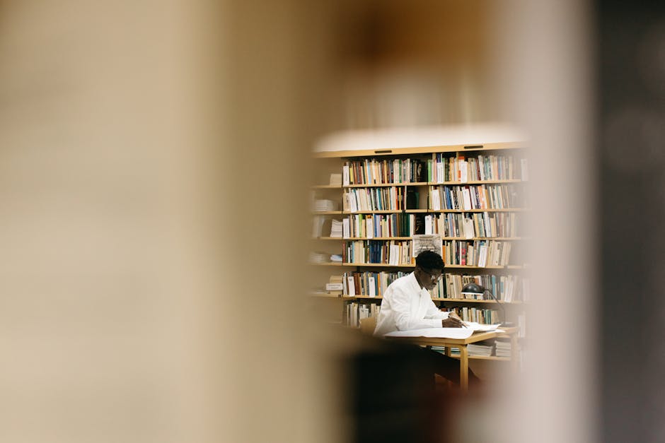 A student intensely focused on work in a library surrounded by bookshelves.
