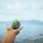 The Migration Arbitrage: How Global Mobility Reshapes Financial Strategy A hand holds a small globe with a scenic ocean backdrop, symbolizing global exploration.
