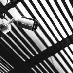 The Panopticon Effect: How Surveillance Shapes Strategic Decision Making Black and white CCTV camera capturing geometric shadows under a modern structure.