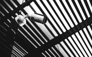 Black and white CCTV camera capturing geometric shadows under a modern structure.