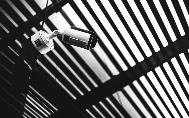 Black and white CCTV camera capturing geometric shadows under a modern structure.