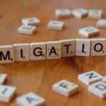 Wooden Scrabble tiles spelling 'Migration' with scattered letters on a wooden table.