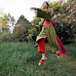 Two people dancing joyfully in traditional wear surrounded by cherry blossoms in a serene Japanese garden.
