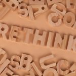 Wooden alphabet letters forming the word rethink on a flat, peach-colored background.