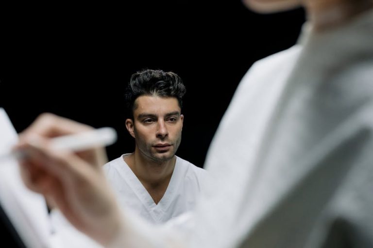 An adult male with a serious expression in a medical environment, observed by a professional taking notes.