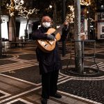 Elderly man playing guitar outdoors at night, surrounded by festive lights. Celebrating music and resilience.