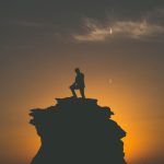 Silhouette of a man standing on a rocky peak with a stunning sunset backdrop in Abu Dhabi.