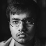 Close-up black and white portrait of a young man with glasses looking serious.
