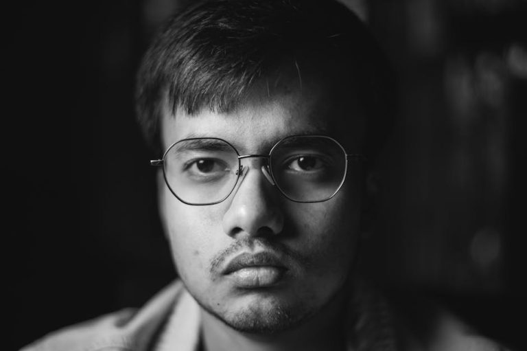 Close-up black and white portrait of a young man with glasses looking serious.