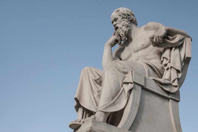 Stone statue of philosopher Socrates sitting in thoughtful pose in Athens, Greece under a clear blue sky.