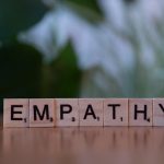 Close-up of tiles spelling empathy on a wooden surface with blurred green background.