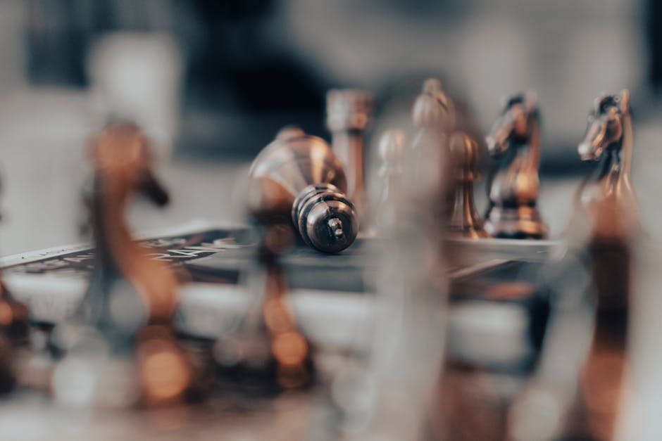 A focused artistic close-up of chess pieces on a board, featuring a fallen king, captured with shallow focus.