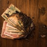 Scorched banknotes scattered on a dark wooden table, symbolizing financial loss.
