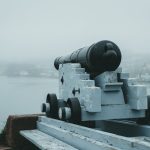 A historic cannon aimed at the misty seaside from a fortress, evoking a sense of defense and history.