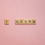 Scrabble tiles spelling 'I Dream' on a soft pink background for motivation.