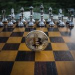 Bitcoin coin standing on a chessboard with silver and brass chess pieces. Concept of strategic digital currency investment.
