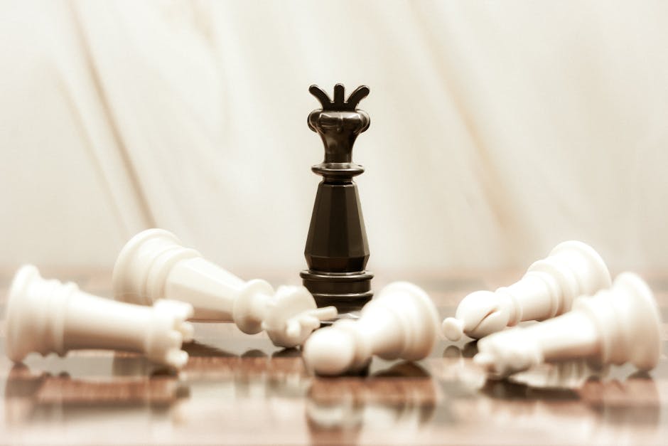 A black chess queen stands triumphant among toppled white pieces on a reflective surface.