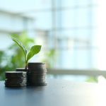 A small plant sprouting from stacked silver coins, symbolizing growth in finance.