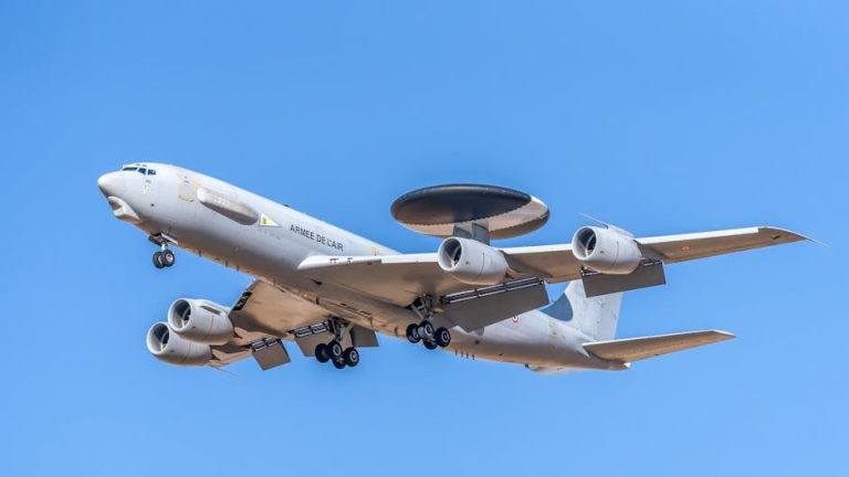 A military AWACS aircraft flying against a clear blue sky, showcasing aerial surveillance capabilities.