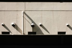 A minimalist wall featuring multiple security cameras casting long shadows in the sunlight.