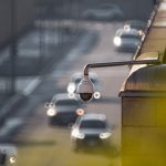 The Surveillance Paradox: Managing Risk in an Age of Total Visibility CCTV camera monitoring city traffic on a busy road with blurred vehicles in the background.