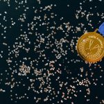 The Toxicity of Success: How Winning Destroys Organizational Culture Close-up of a gold medal with blue ribbon and confetti on a black surface, symbolizing victory.