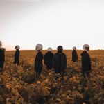 The Trauma-Performance Paradox: How Artists Optimize Suffering A group of people in astronaut helmets standing in a field of yellow flowers at sunset.