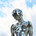 The Trauma Tax: Why Futurism Fails Without Psychological Resilience A sleek chrome robot sculpture stands against a bright blue sky background.