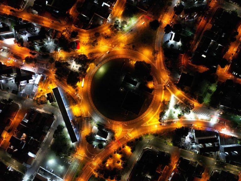 A stunning aerial view of a city roundabout lit up at night with vibrant streetlights and traffic.