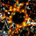 A stunning aerial view of a city roundabout lit up at night with vibrant streetlights and traffic.