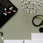 Medical workspace with laptop, molecules, and stethoscope on green background.