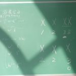Algebra equations with symbols on a chalkboard in a brightly lit classroom.
