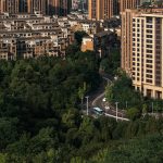 Aerial photo showcasing urban residential buildings surrounded by lush green trees, featuring a winding road below.