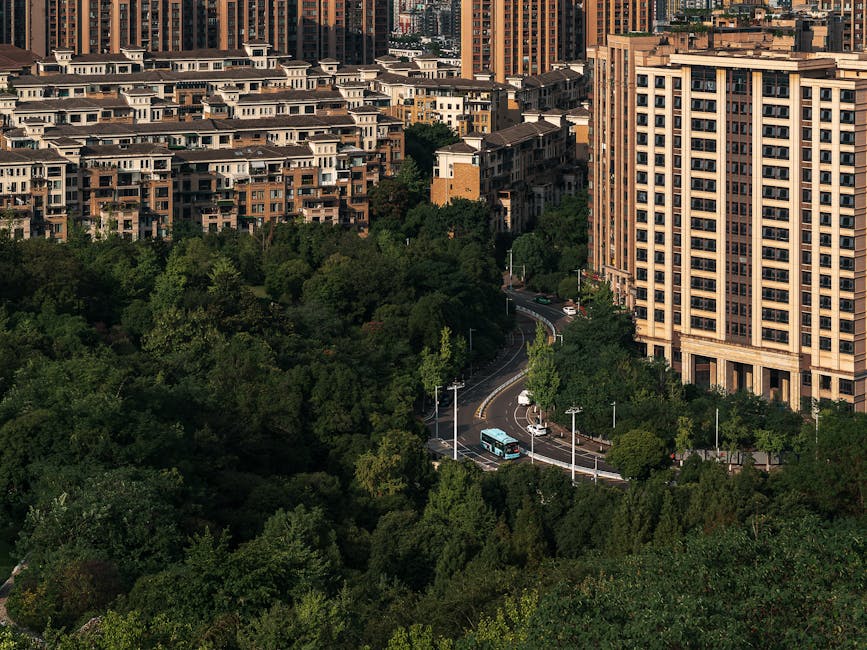 Aerial photo showcasing urban residential buildings surrounded by lush green trees, featuring a winding road below.