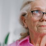 Why Aging is the Ultimate Constraint for Strategic Futurism Close-up portrait of a thoughtful elderly woman wearing glasses indoors.