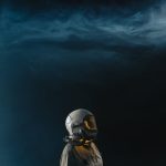 Astronaut in a helmet looks toward the stars in a mysterious space setting.